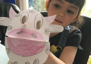 Dziewczynka pokazuje zrobioną z papieru krowę z zamkniętą mordką